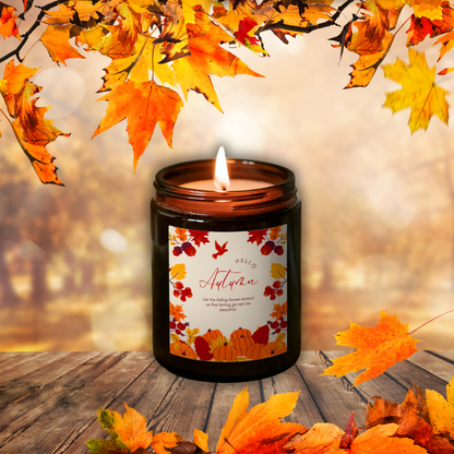 Lumânare Pumpkin Spice aprinsă, în borcan maro, cu eticheta „Hello Autumn”, printre frunze de toamnă pe o masă de lemn