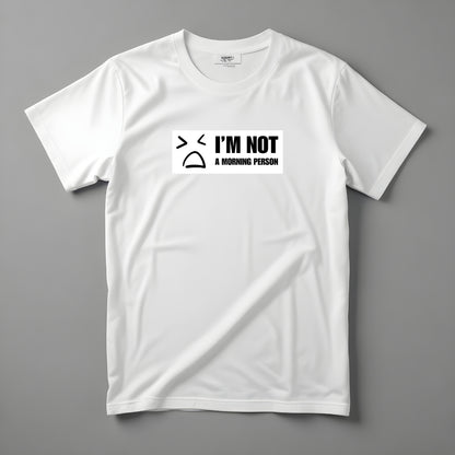 Tricou Kiskedves I'm not a morning person cu o figură desenată îmbufnată și textul I'M NOT A MORNING PERSON, fotografiat întins.