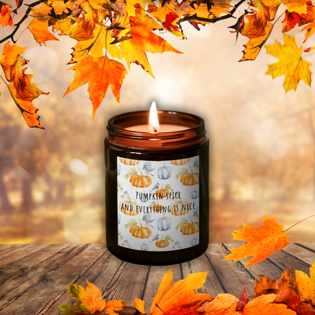 Lumânare Pumpkin Spice aprinsă, în borcan maro, cu eticheta „Pumpkin spice and everything is nice”, printre frunze de toamnă pe o masă de lemn