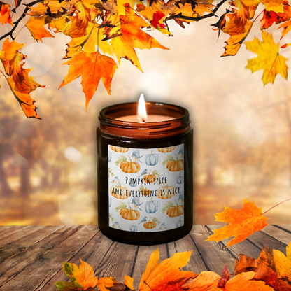Lumânare Pumpkin Spice aprinsă, în borcan maro, cu eticheta „Pumpkin spice and everything is nice”, printre frunze de toamnă pe o masă de lemn