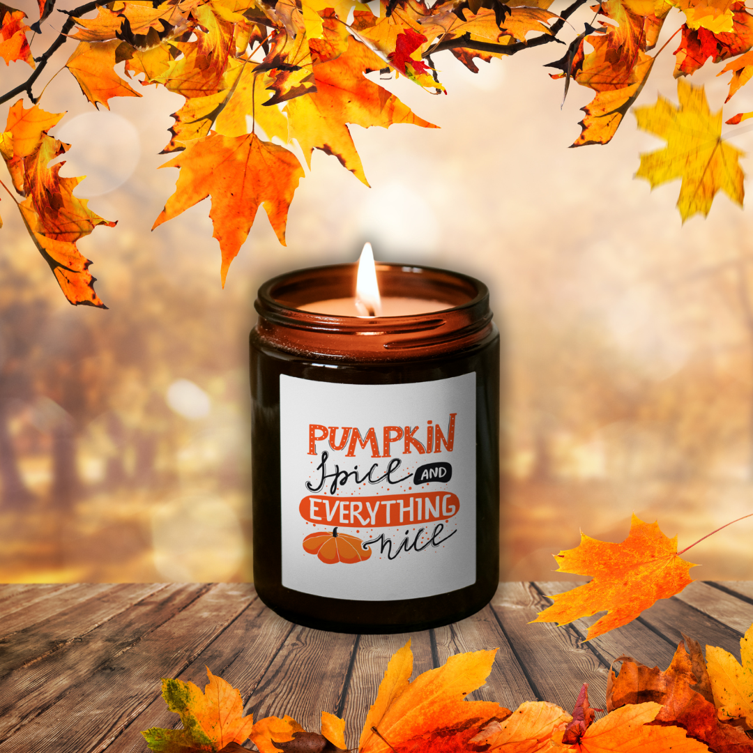 Lumânare Pumpkin Spice aprinsă, în borcan maro, cu eticheta „Pumpkin Spice and everything nice”, printre frunze de toamnă pe o masă de lemn