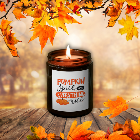 Lumânare Pumpkin Spice aprinsă, în borcan maro, cu eticheta „Pumpkin Spice and everything nice”, printre frunze de toamnă pe o masă de lemn