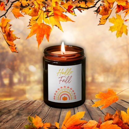Lumânare din ceară de soia Pumpkin Spice aprinsă, în borcan maro, cu eticheta „Hello Fall”, printre frunze de toamnă pe o masă de lemn