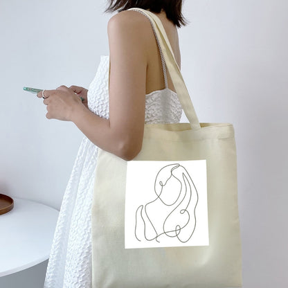 Sacoșă de pânză Kiskedves Line Art pe umăr, cu siluete împletite, la o rochie albă de vară.