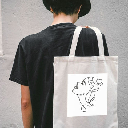 Sacoșă de pânză Kiskedves Line Art purtată pe spate, chip cu floare în păr, pe o persoană în tricou negru.