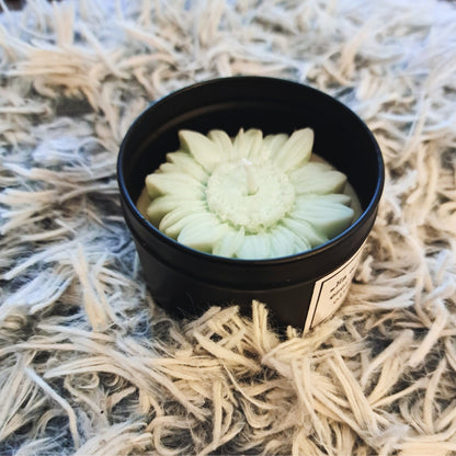 Lumânare din ceară de soia Kiskedves cu floare, în cutie metalică neagră, cu floare de ceară verde pastel, pe un covor moale