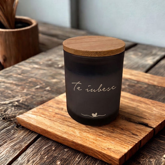 Lumânare decorativă personalizabilă Ocean în sticlă neagră mată cu capac de bambus, cu textul „Te iubesc” și o inimioară, pe un tocător de lemn