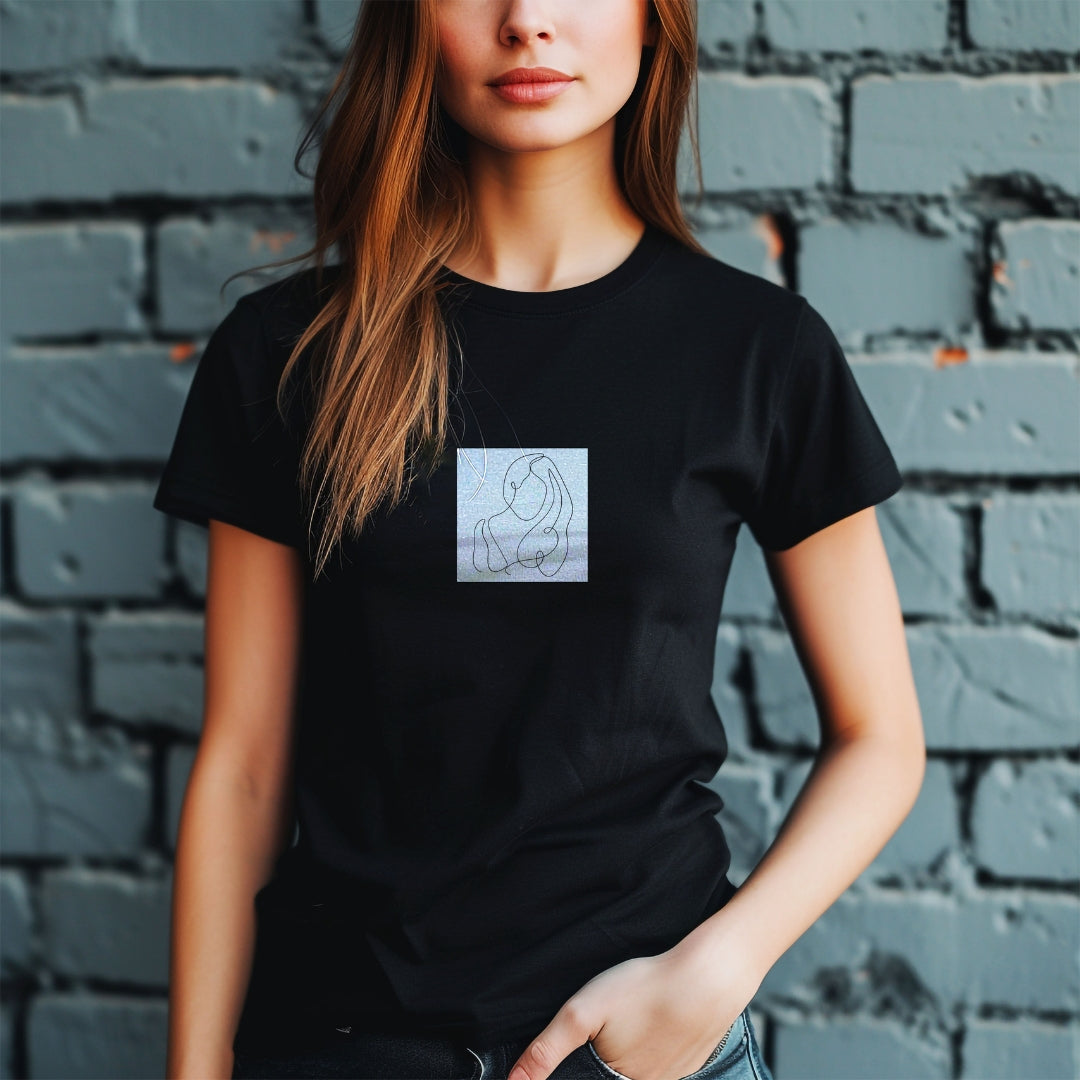 Tricou negru Kiskedves Line Art cu siluete împletite, pe o modelă, în fața unui zid de cărămidă.