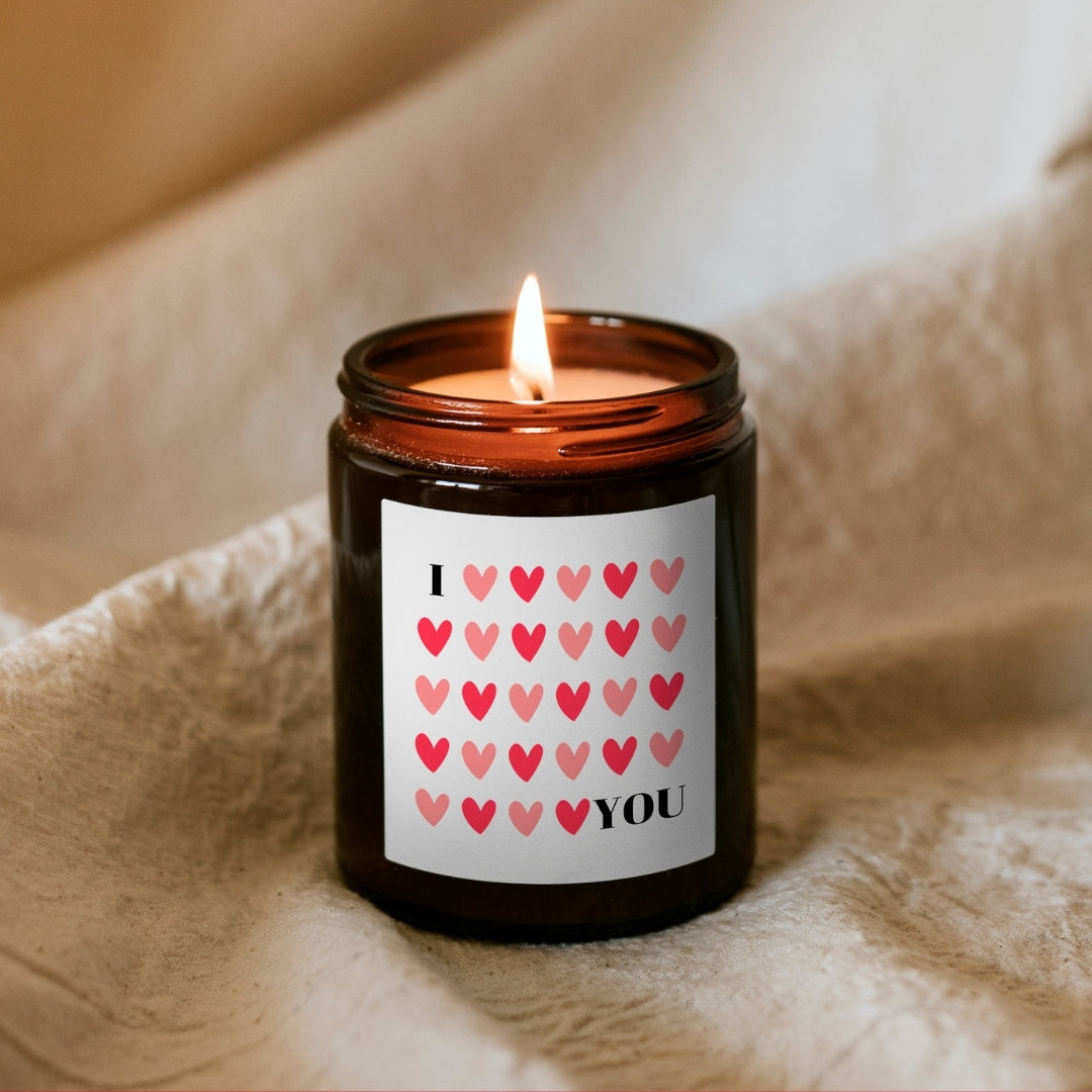Lumânare Kiskedves I ❤️ YOU aprinsă, din ceară de soia, în borcan maro, cu etichetă cu inimioare roșii și roz.