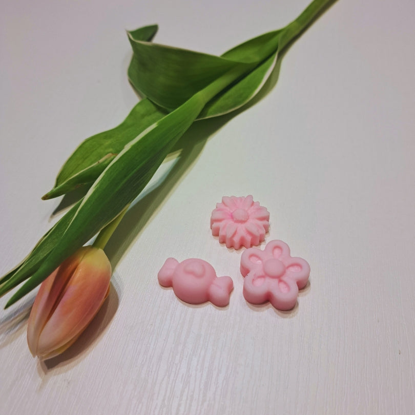 Set de ceară parfumată de primăvară Kiskedves: iepuraș roz, margaretă și floare pe o masă albă de lemn, alături o lalea.