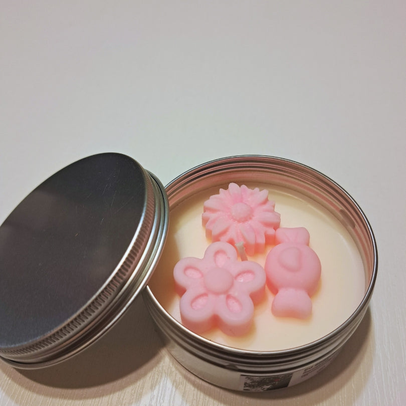 Lumânare de primăvară Kiskedves în cutie metalică argintie, cu capacul dat la o parte și floricele roz din ceară