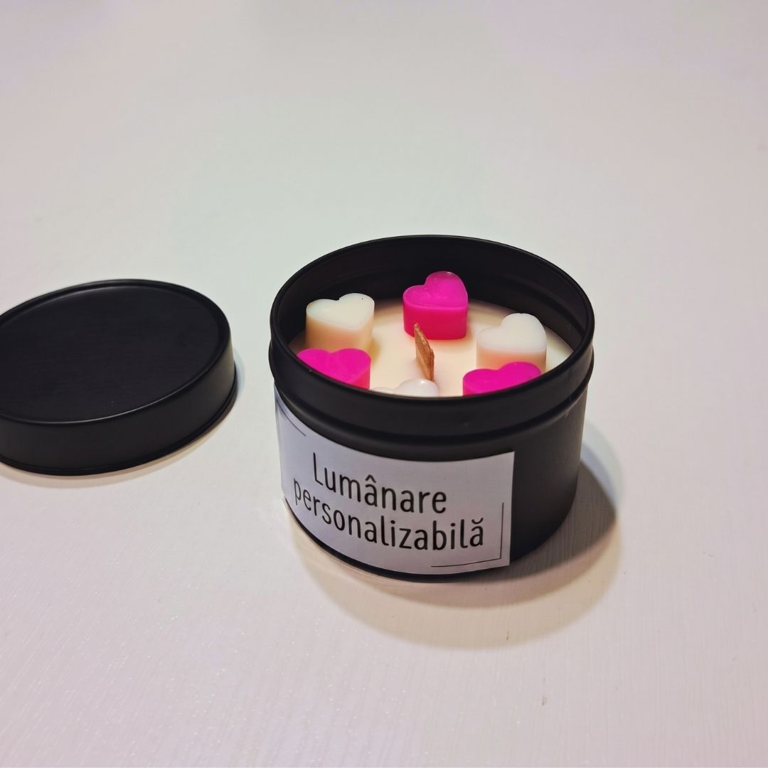 Lumânare din ceară de soia cu fitil de lemn în cutie metalică neagră, cu inimioare de ceară roz și albe și eticheta „Lumânare personalizabilă”, alături capacul cutiei
