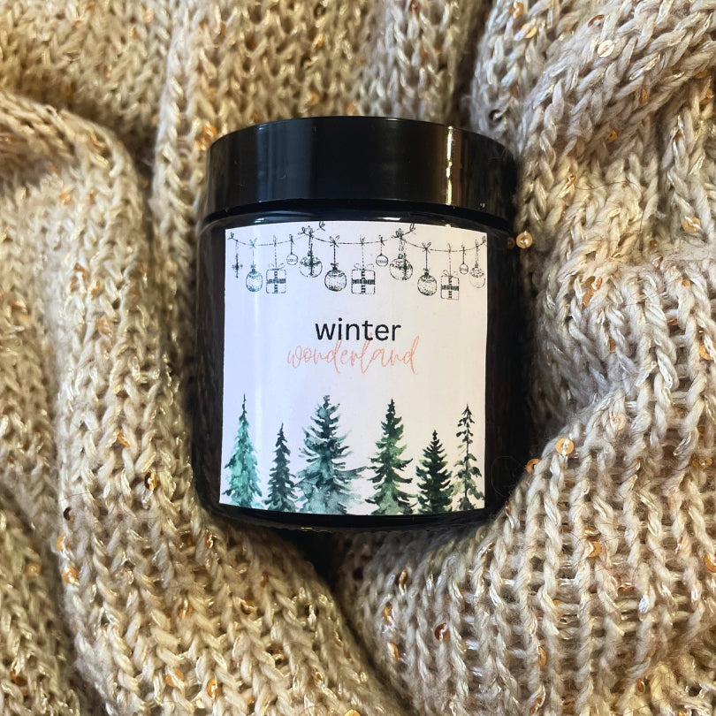 Lumânare Kiskedves Winter Wonderland pe o pătură tricotată, se vede bine eticheta acuarelă cu brazi.